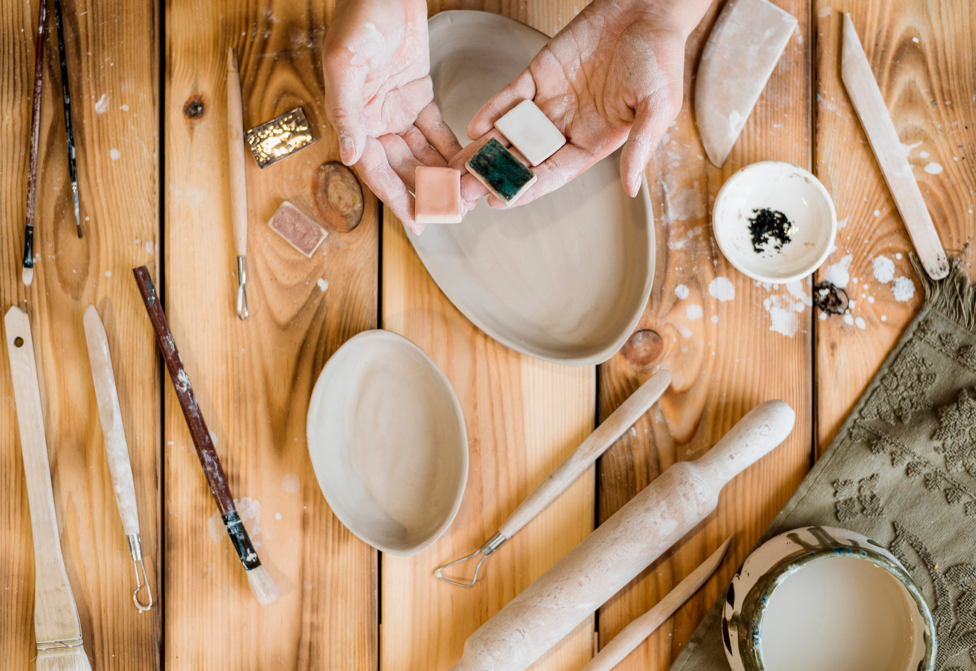 Pottery tools and glaze test tiles laid out on a wood studio table
